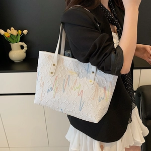 White quilted tote bag with colorful embroidery and gold rivets shown on a model