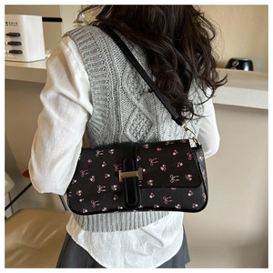Détail du sac baguette floral noir avec boucle dorée porté par un mannequin