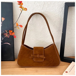 Detail of caramel suede baguette bag with ribbon bow, set against artistic background