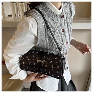 Détail du sac baguette noir avec imprimé floral rose et boucle dorée en forme de H