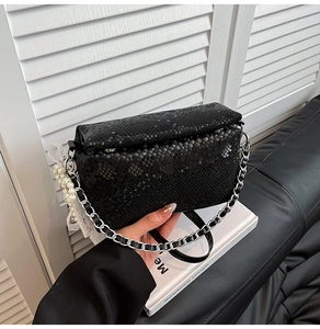 Close-up of black snakeskin pattern bag with silver chain and elegant pearl lace charm
