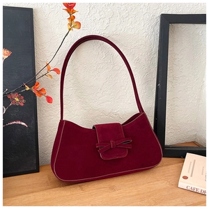 Detail of vintage burgundy suede shoulder bag with elegant bow flap on a stylish table
