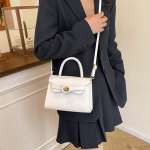 Minimalist white leather trapezoid handbag with gold clasp worn by model in a suit