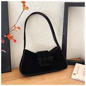 Close-up of black suede baguette bag featuring a decorative bow and thin shoulder strap