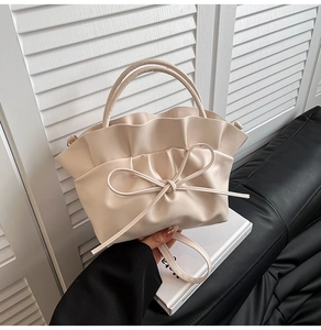 Detail of beige pleated cloud bag with ribbon bow and smooth top handles in soft light