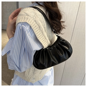 Detail of black cloud pleated baguette bag with glossy soft leather texture and slim strap