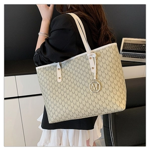 Detail of large tote bag with M-pattern print and golden metal charm on white leather