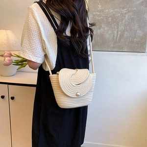 Beige woven crossbody bag with large pearl clasp shown on a model in natural light