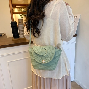 Green hand-woven cotton rope crossbody bag with pearl buckle shown on model in cafe