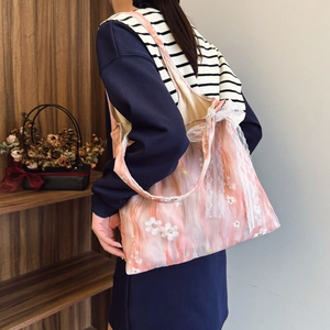 Pink floral embroidery tote bag with white lace bow detail worn by a model in soft light