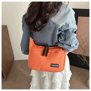 Detail of orange nylon shoulder bag featuring dual zippers and Fashion text logo decoration