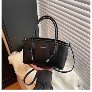 Détail du sac à main noir montrant le texte 'FASHION' et des finitions nouées