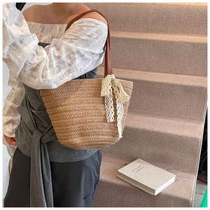 Detail of hand-woven straw tote with brown leather strap and white lace bow detail