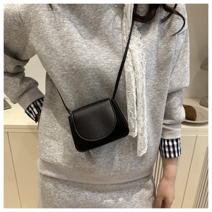 Close-up of a mini black crossbody bag worn by a model in a stylish indoor setting