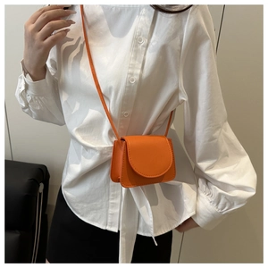 Close-up of orange mini crossbody bag with litchi grain texture on white shirt