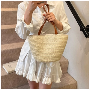 Detail of hand-woven straw tote bag with brown leather straps and beige woven texture