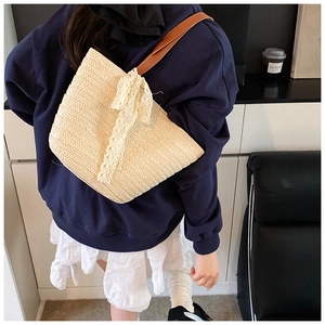 Detail of cream hand-woven straw shoulder bag featuring a delicate white lace bow accent
