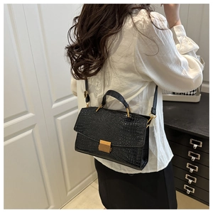 Detail of black glossy crocodile pattern leather with gold metal buckle on top handle bag