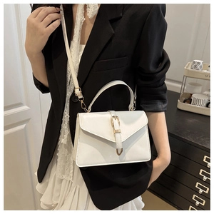 Détail d'un sac bandoulière blanc style enveloppe avec boucle dorée sur un blazer noir