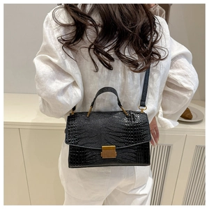 Detail of black crocodile texture handbag with gold buckle on a shoulder strap