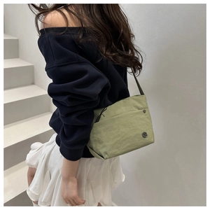 Olive green nylon crossbody bag detail with metallic rivet and circular logo emblem