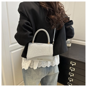 Detail of silver sequin crossbody bag with a hard top handle worn by a model in a suit