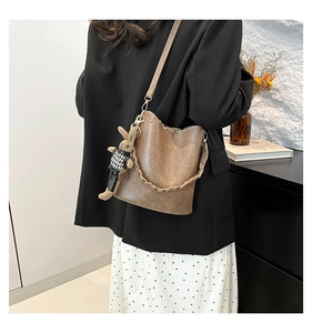 Brown bucket bag featuring woven handle and cute rabbit charm on a model in modern home setting