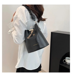 Detail of black faux leather bucket bag featuring a wide woven strap and gold hardware