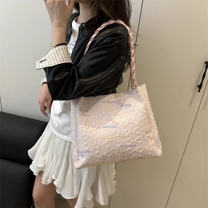 Pale pink quilted tote bag with multicolor embroidery and woven handles on a model