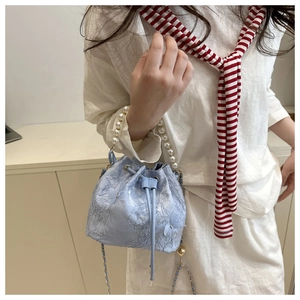 Detailed macro view of light blue lace bucket bag with pearl handle and floral embroidery