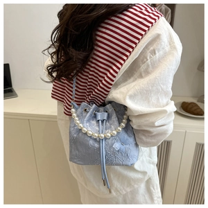 Macro shot of light blue bucket bag with 3D floral texture and elegant pearl handle
