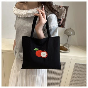 Detailed close-up of apple embroidery on a black nylon tote bag with model lifestyle shot
