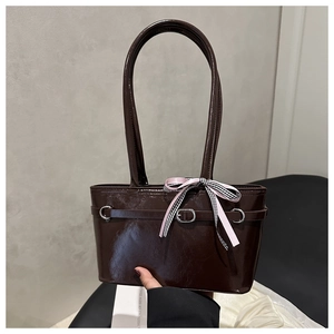 Detail view of glossy brown patent leather shoulder bag with decorative pink ribbon bow