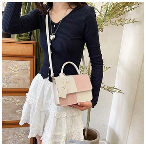 Detail of a pink and cream crossbody bag with top handle shown in a cozy indoor setting