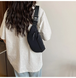 Detailed back view of a minimalist black nylon crossbody bag worn by a female model