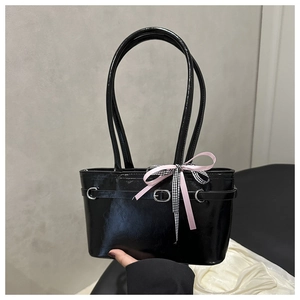 Detail of glossy black patent leather bag with a pink bow and silver buckle accent