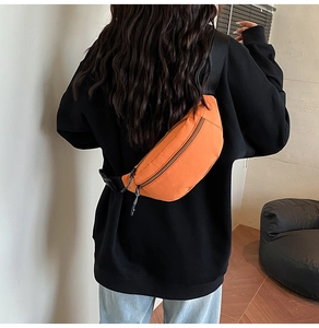 Macro shot of a bright orange crossbody waist bag on a model in black hoodie clothing