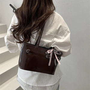 Brown glossy patent leather tote bag with bow ribbon detail on minimalist stairs