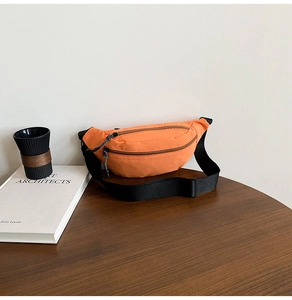 Detail of bright orange sports waist bag with dual zippers and adjustable black strap