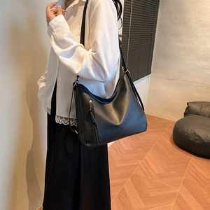 Minimalist black leather tote bag with vertical zipper and tassel detail worn by model