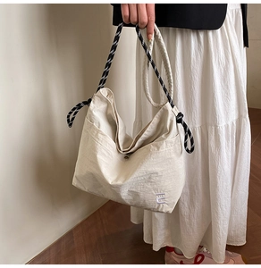 Detail view of cream nylon tote bag with black and white striped rope handles and embroidery