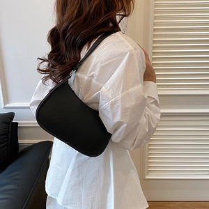 Minimalist black pebble leather baguette bag shown as worn on shoulder over white shirt