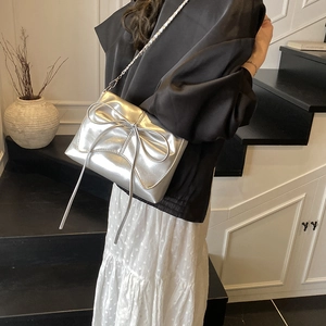Metallic silver bow shoulder bag with sleek metal chain strap shown on model outdoors