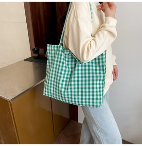 Close-up of a large green gingham tote bag with tie closure on a female model shoulder