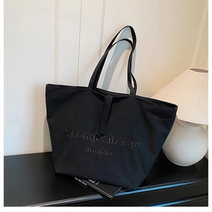 Detail of minimalist black canvas tote bag with 3D embroidery and wide shoulder strap