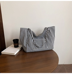 Detailed view of striped canvas tote bag with front pocket on a wooden table