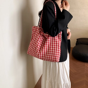 Red gingham canvas tote bag with bow detail worn by model in a minimalist setting