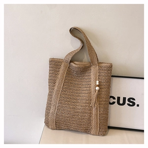 Detail of woven straw tote bag featuring decorative tassels and white wooden beads