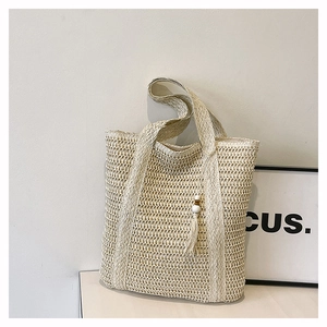 Detail of hollow woven texture and wooden bead tassel on cream straw shoulder bag