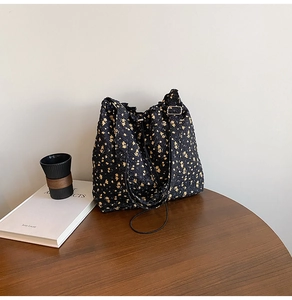 Close-up of black floral jacquard tote bag with adjustable strap on wooden table